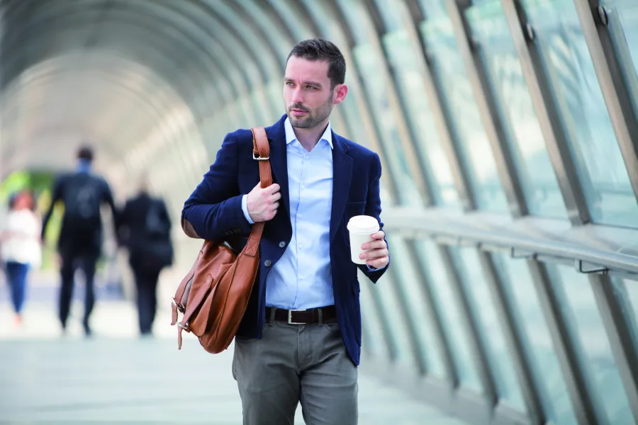 Junger mann mit Schultertasche und Getränkebecher in Passerelle